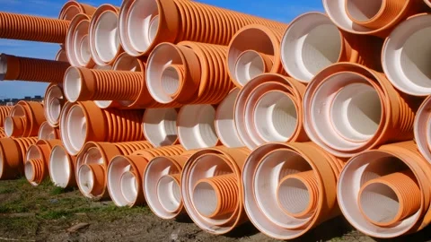 Camera moving right showing stacked orange corrugated drainage pipes Stock Footage 296749428