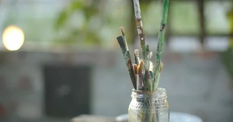 Camera is moving upward, pulling focus and revealing painted brushes in glass Stock Footage 344255076