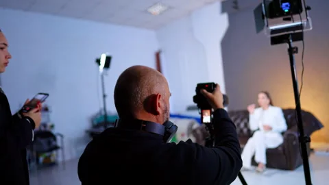 Camera Operator Filming Interview In Photo Studio. Camera operator films seated Stock Footage 334812837