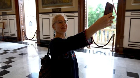 Camera orbits around a mature middle aged tourist woman holds up her smartphone Stock Footage 129886969