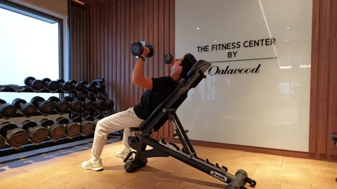 Camera orbits left around a man lifting dumbbells on an incline bench in a Видео 335395061