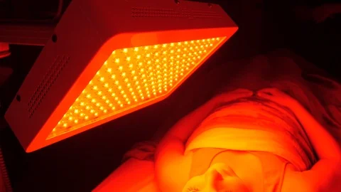 Camera pan as client sitting under infrared lamp to the left Stockbeeldmateriaal 107760128