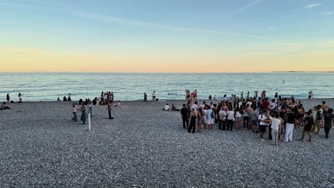Camera pan right of a crowd gathered on a pebble beach at sunset Stock Footage 336922929