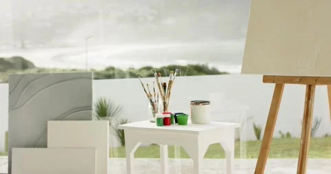 Camera is panning across stack canvases and easel with paint pots and brushes, Stock Footage 344317385