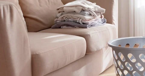 Camera is panning beige sofa with folded laundry near window as daylight is Stock Footage 343888808