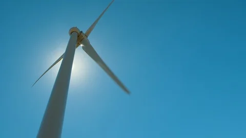 Camera panning left-to-right on wind tower silhouetted against the sun. Stock Footage 87888024