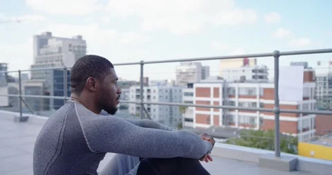 Camera panning, man sitting on rooftop near railing, wearing grey top, holding Stock Footage 337944044