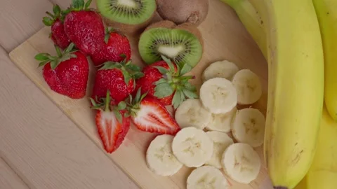 Camera panning over fresh strawberries kiwi and banana slices on cutting board 스톡 동영상 343228835