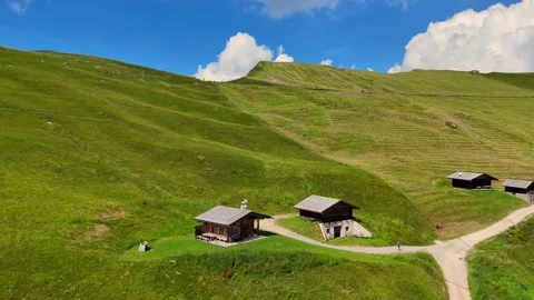 Camera panning over green hills with wooden huts showing tourists hiking Stock Footage 285085800