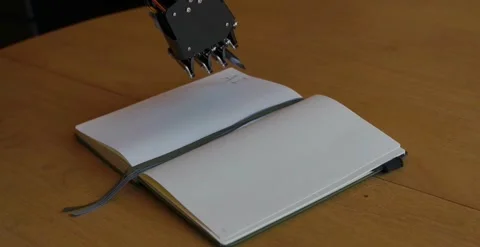 Camera Panning Of Robotic Hand After Writing AI on a Notebook Stock Footage 248090155