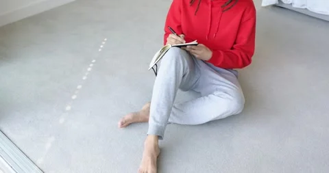 Camera panning upward from bare feet is revealing person pausing with pen and Stock Footage 334999622