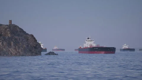 Camera pans along headland to reveal oil tanker ships anchored in bay at sunset Stock Footage 334040217