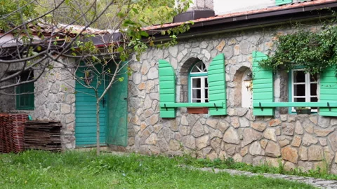 Camera pans along rustic stone cottage with green shutters and ivy covered wa Stock Footage 346799266
