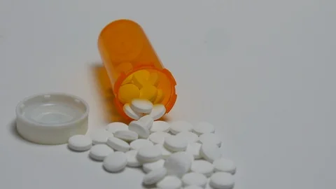 Camera pans to a bottle of pills spilling out onto white surface. Stock Footage 108033483