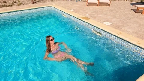 Camera pans down to a woman getting into swimming pool on a nice day Stock Footage 163609806