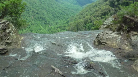 Camera Pans Up from Edge of Waterfall to Reveal Lush Green Valley Stock Footage 314449577