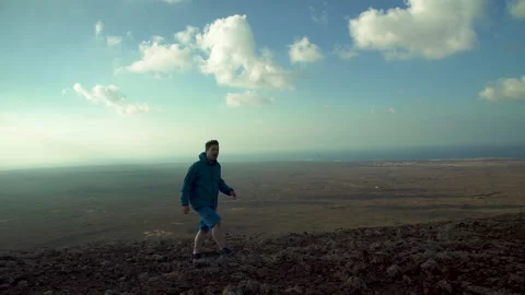 Camera pans with hiker walking up to rim of volcano in desert landscape Stock Footage 141607185