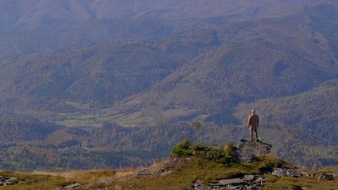 Camera pans from a man in a coat standing on a rock at the edge of a mountain. Video stock 235376839