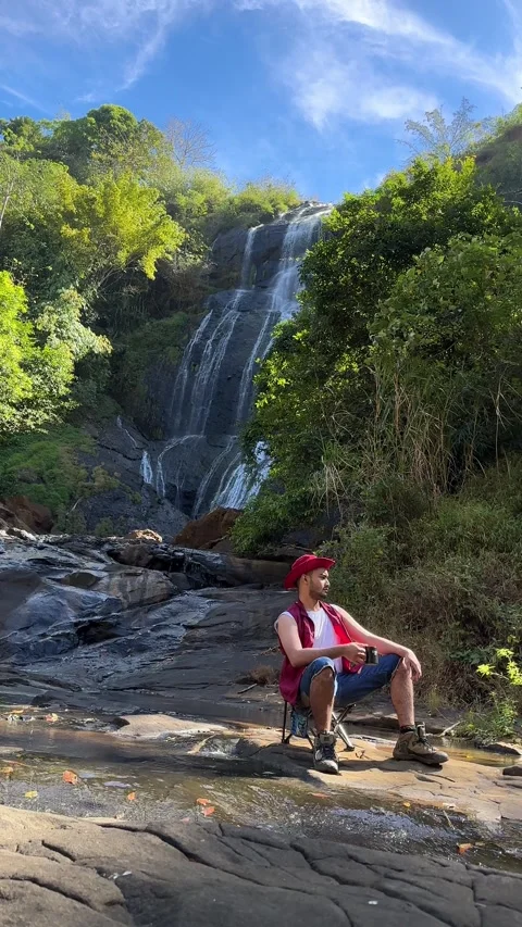 Camera Pans Up to Reveal Man Sitting by Waterfall in Tropical Forest, Vertical S Stock Footage 324772848