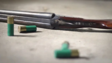 Camera pans by shotgun shells lying on concrete floor near double barrel shotgun Stock Footage 75013561