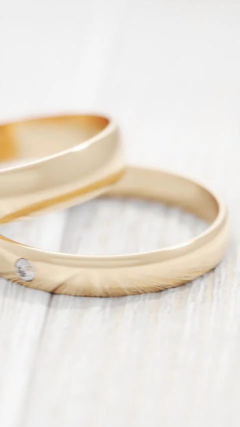Camera pans sideways past two gold wedding rings on a white wooden table. Stock Footage 250198358