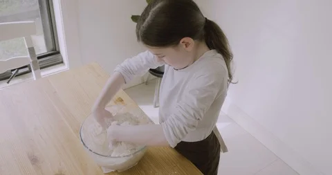 Camera pans from slightly overhead as child kneads and mixes bread dough by hand Video stock 115480405