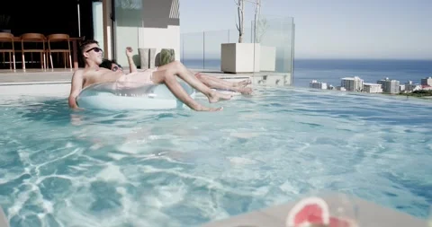 Camera pulling back, African American men relaxing in rooftop pool on float, Stock Footage 344254653
