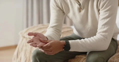 Camera pulling back, African American man rubbing hands self-soothing on bed in Stock Footage 346615552