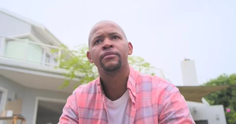 Camera pulling back, African man in plaid sitting up, looking off-frame and Stock Footage 341468437