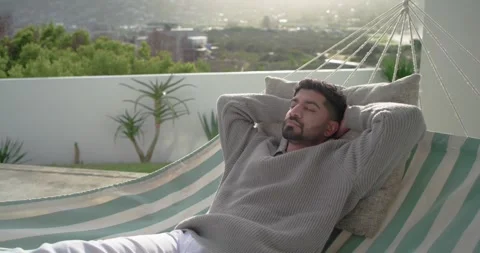Camera pulling back man reclining in hammock on terrace with cushion revealing Stock Footage 342233385