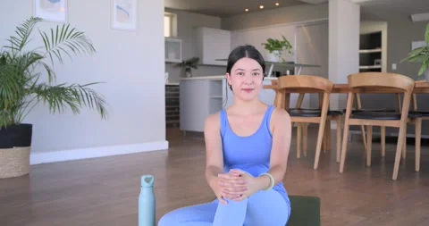 Camera pulling back revealing Asian woman in activewear sitting on mat, greeting Stock Footage 341468523