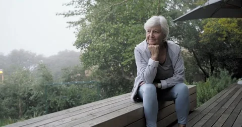 Camera pulling back, revealing senior woman resting chin on fist on deck bench, Stock Footage 337287311