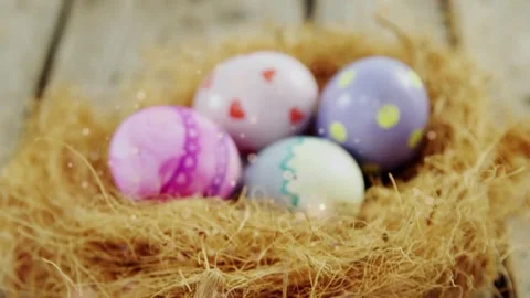 Camera pulling back, revealing straw nest with four pastel eggs, sparkles Stock Footage 330508819