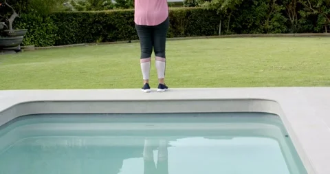 Camera pulling back revealing woman standing on pool edge, raising arms Stock Footage 341665153