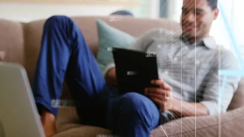 Camera pulling back showing man tapping tablet viewing tech data while binary Video stock 333425950