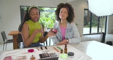 Camera pulling back showing woman host demonstrating blush with brush at desk Stock Footage 342595787