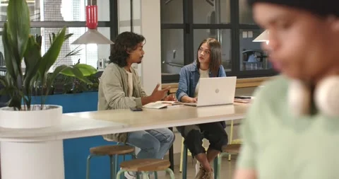 Camera pulling back two peers working at table, gesturing, typing on laptop, Stock Footage 339272239