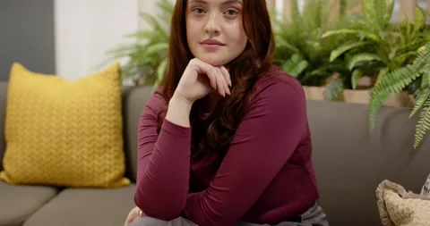 Camera pulling back, woman sitting on gray sofa lifting head, smiling toward Stock Footage 339679832