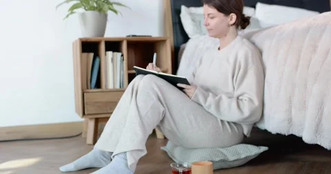 Camera pulling back woman wearing sweater sitting on cushion beside bed Stock Footage 348222649