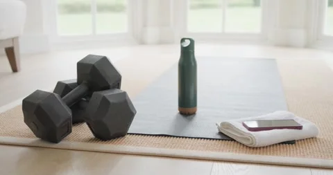 Camera pulling back on wood floor by windows, revealing dumbbells, bottle, towel Vídeos de archivo 341394288