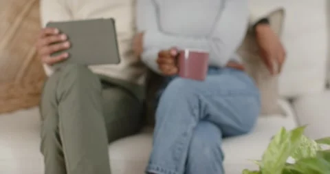 Camera pulling focus couple leaning on sofa, man scrolling tablet, woman holding Stock Footage 346644531