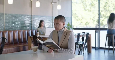 Camera pulling focus, revealing African American woman reading book for study at Stock Footage 344671681