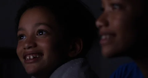 Camera pulls focus between two children watching a screen together at night Stock Footage 114388418