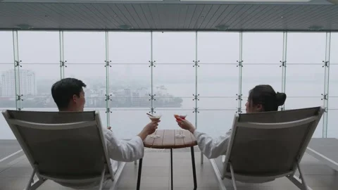 Camera pushes in on a couple toasting cocktails by an indoor infinity pool with 库存影片 335381237