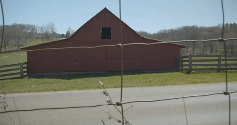 Camera pushes through fence with barn and car passing Stock Footage 128826629