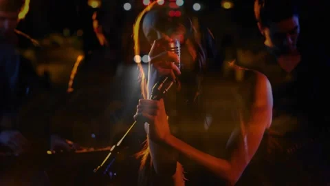 Camera revealing female singer singing holding chrome mic taillight bokeh Stock Footage 332289107