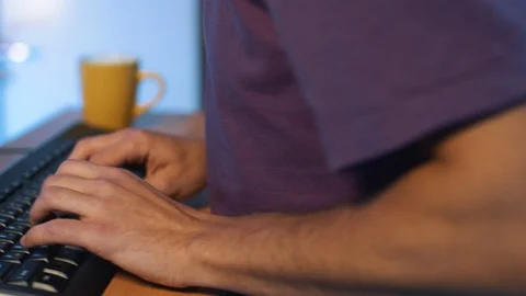 Camera revolves around hands of man in purple t-shirt typing on black keyboard Stock Footage 119347230