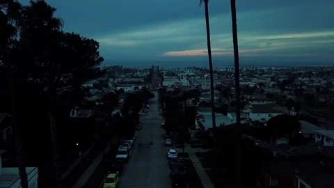 Camera rises to reveal cloudy dark beach town with palm trees Stock Footage 84774199