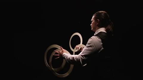Camera rotates around focused man twisting white circus rings to juggle. Juggler Stock Footage 147124377
