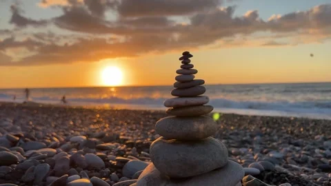 Camera rotates around pyramid of small stones on pebble beach on sunset Stock Footage 263447755